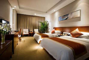 Een hotelkamer met twee bedden, een bureau met stoel, een televisie en een groot raam.