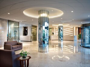 A modern lobby with a central glass elevator, seating area, and a reception desk. - Nanjing Expo Center Hotel (Nanjing)
