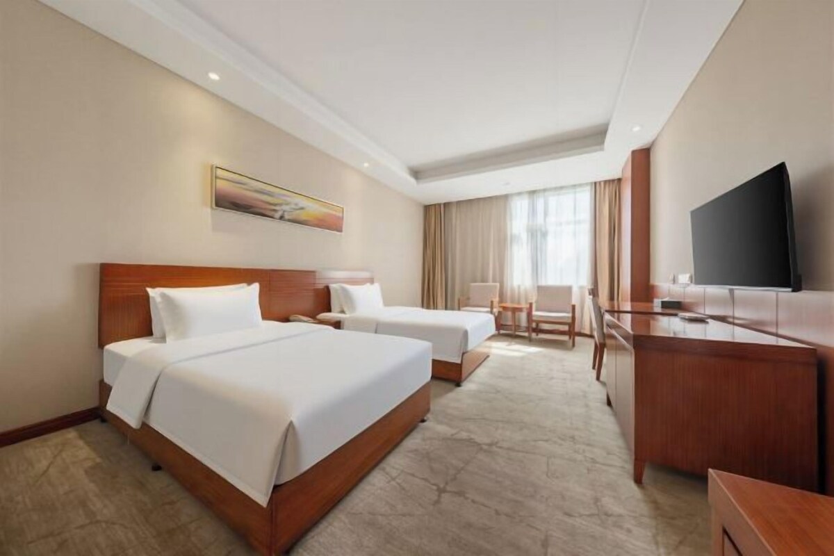A hotel room with two beds, a desk, a TV, and a window with curtains.