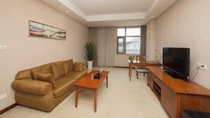A living room with a sofa, a coffee table, a TV, and a window with curtains. - Nanjing Expo Center Hotel (Nanjing)