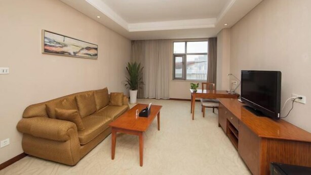 A living room with a sofa, a coffee table, a TV, and a window with curtains. - Nanjing Expo Center Hotel (Nanjing)
