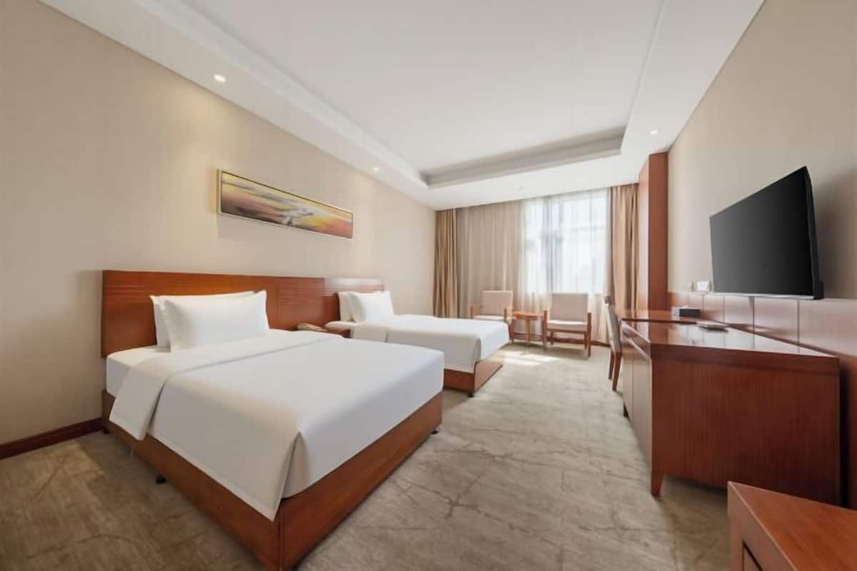 Une chambre d’hôtel avec deux lits, un bureau, une chaise, une télévision et un tableau au mur.