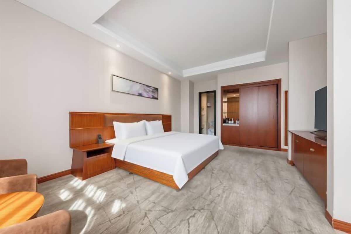 Une chambre d’hôtel comprenant un lit, une tête de lit en bois, des tables de chevet, un téléviseur et une armoire.