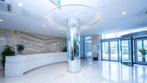 Un hall d’entrée moderne avec une colonne centrale en verre, un comptoir d’accueil et de grandes fenêtres.