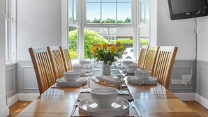 Comedor con mesa de madera dispuesta para seis personas, platos, cuencos y cubiertos blancos.