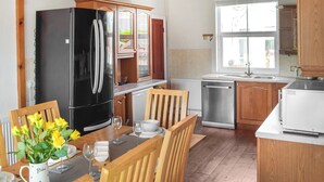 Una cocina moderna con armarios de madera, un refrigerador negro, lavavajillas y una mesa de comedor con sillas y un jarrón de flores amarillas.