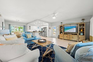 A spacious living room with a large TV, a dining area, and a kitchen in the background. - Jamaica Royale Beach View Tower by Beachside Management (Siesta Key)