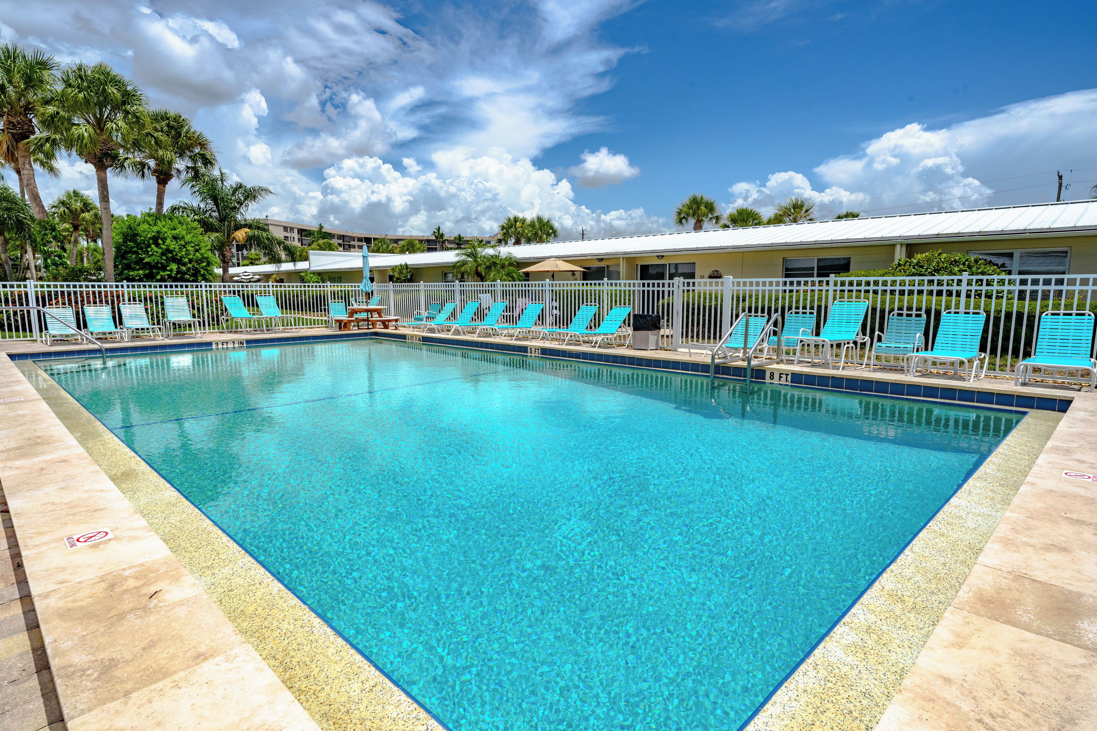 A clear blue pool with lounge chairs and a white fence.