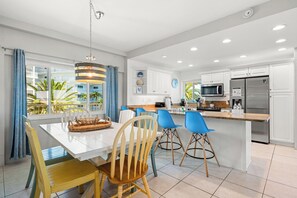 A modern kitchen with white cabinets, a stainless steel refrigerator, and a dining area with a white table and chairs. - Jamaica Royale Beach View Tower by Beachside Management (Siesta Key)