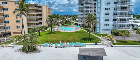 A resort with multiple-story buildings, a swimming pool, and a sandy beach area with lounge chairs.
