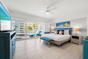 A spacious bedroom with a large bed, a ceiling fan, a TV, and a balcony with a pool view. - Jamaica Royale Beach View Tower by Beachside Management (Siesta Key)