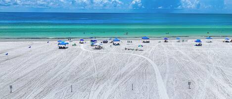 A beach with clear blue water, white sand, and blue umbrellas.