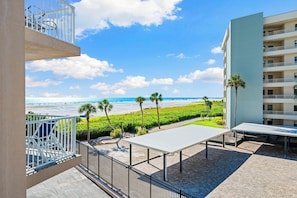 A balcony with a view of the beach and ocean, a white table, and a building with multiple balconies. - Jamaica Royale Beach View Tower by Beachside Management (Siesta Key)