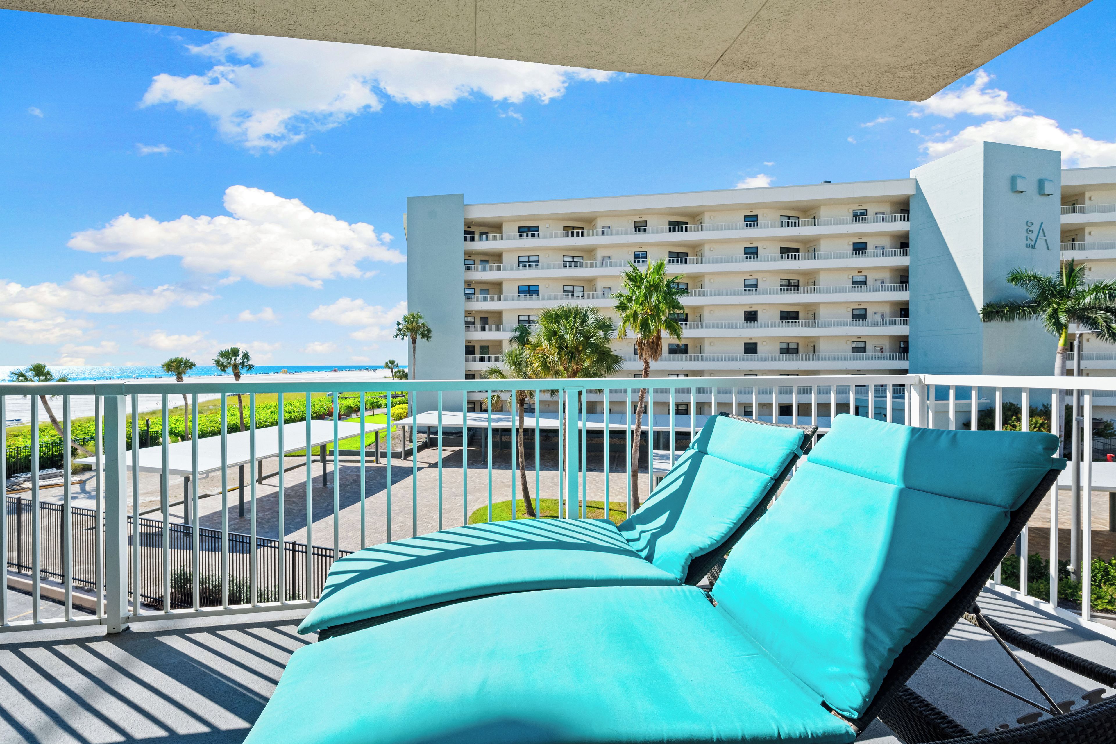 A balcony with turquoise lounge chairs and a view of a hotel building with multiple balconies.