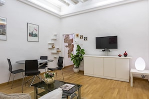 A modern living room with a dining area, a TV, a plant, and artwork on the walls. - Charming Santo Spirito 1bdr apartment (Firenze)