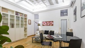 Uma sala de estar moderna com uma mesa de vidro, cadeiras pretas, um sofá branco, estante e um claraboia.