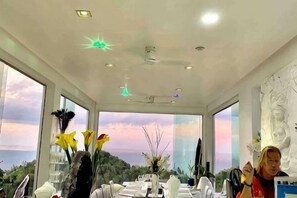 A modern dining area with a view of the landscape, a ceiling with recessed lighting, and a statue on the wall. - Best World Vision (Koh Samui)