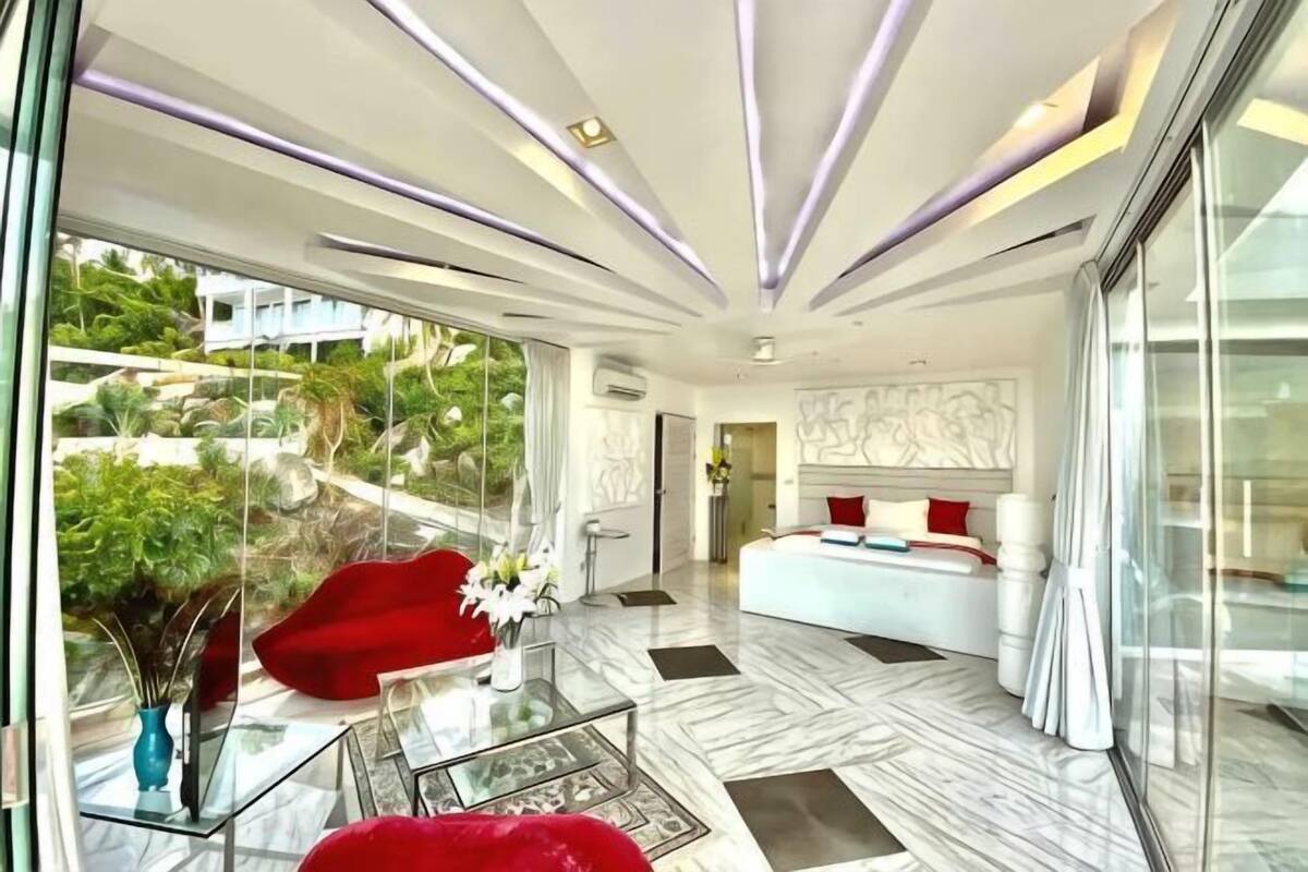Um interior moderno com parede de vidro, sofá vermelho, cama branca e chão de mármore.