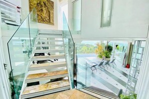 A modern staircase with glass railings leading to an outdoor patio area with a table and chairs. - Best World Vision (Koh Samui)