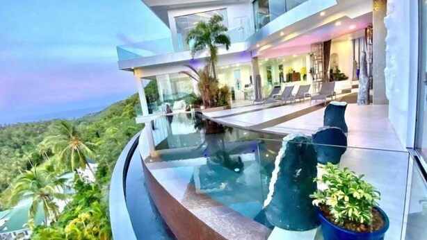 A modern house with a glass infinity pool, outdoor seating, and a view of the surrounding greenery. - Best World Vision (Koh Samui)