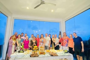 A group of people standing in a room with a large table filled with food items. - Best World Vision (Koh Samui)