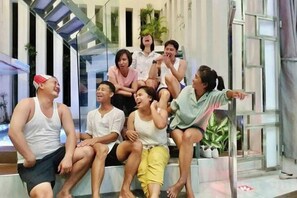 Un grupo de personas sentadas en una escalera en un espacio interior moderno con barandas de vidrio y plantas.