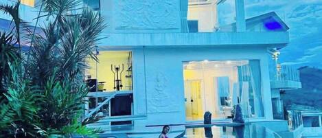 Un edificio moderno con piscina, balcón en el segundo piso y una entrada amplia.
