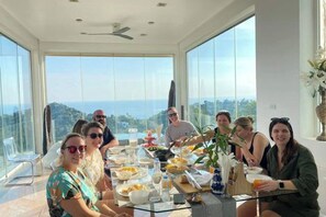 A group of people dining at a table with a large window view of the ocean. - Best World Vision (Koh Samui)