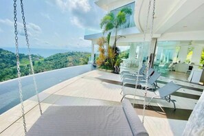 A modern outdoor seating area with a swing chair, a pool, and a view of the ocean. - Best World Vision (Koh Samui)