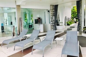 A modern interior with lounge chairs, a glass wall, and a staircase leading to an outdoor area. - Best World Vision (Koh Samui)