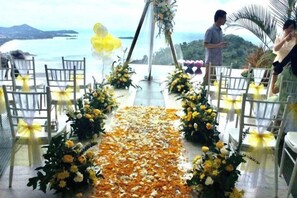 An outdoor wedding ceremony with chairs arranged in a semi-circle, a flower-decorated aisle, and a scenic view of the sea. - Best World Vision (Koh Samui)