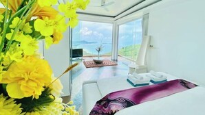 A modern hotel room with a large bed, a view of the sea, and a balcony with a dining table and chairs. - Best World Vision (Koh Samui)