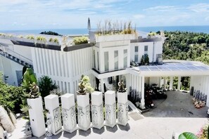 A modern building with a white facade, solar panels, and a covered outdoor area with plants. - Best World Vision (Koh Samui)