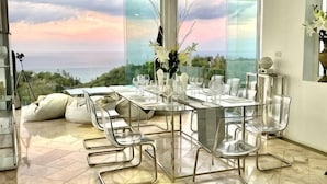 A dining area with a table set for four, clear chairs, and a view of the ocean. - Best World Vision (Koh Samui)