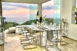 Un comedor con una mesa dispuesta para cuatro personas, sillas transparentes y vista al océano.