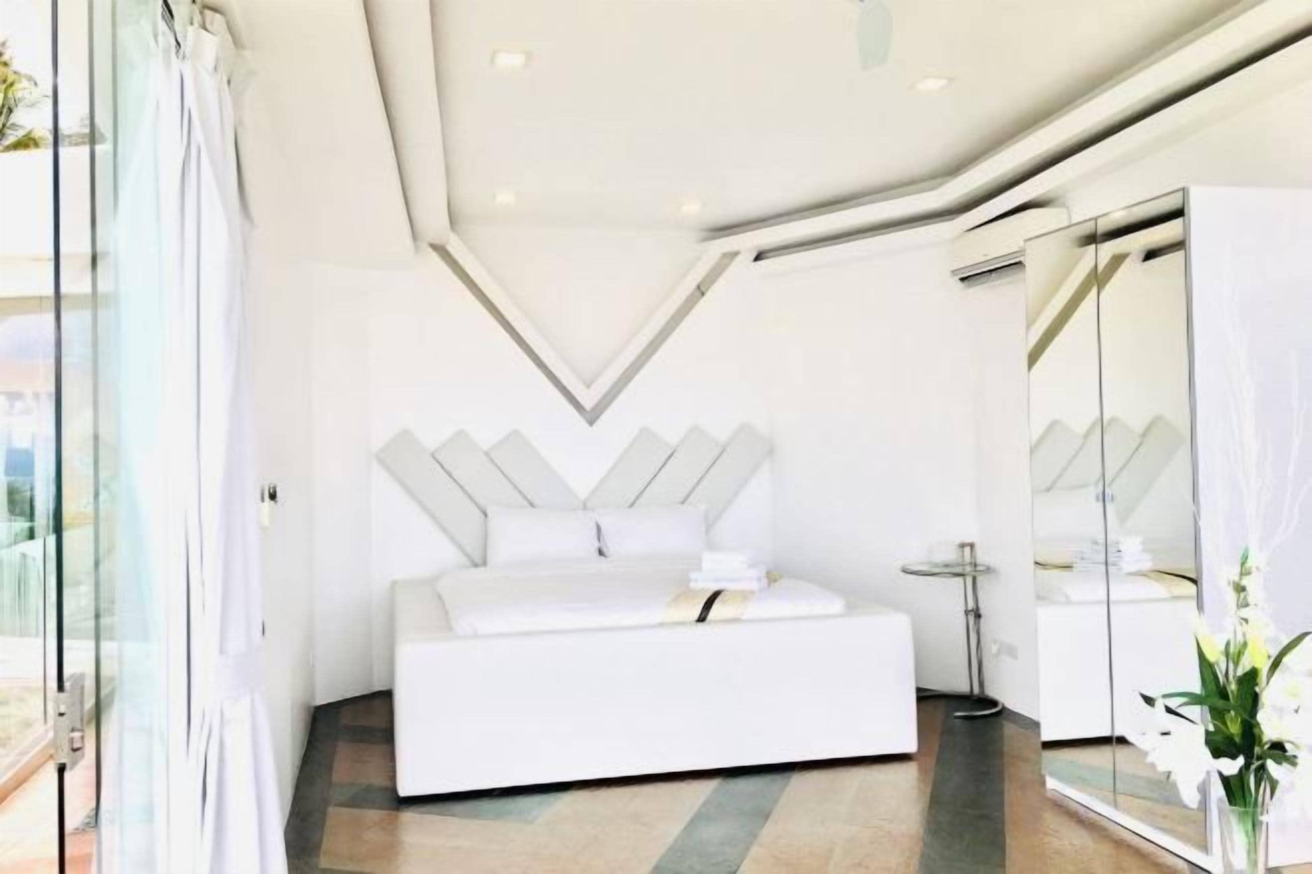 A modern bedroom with a white bed, a glass door, and a large mirror.