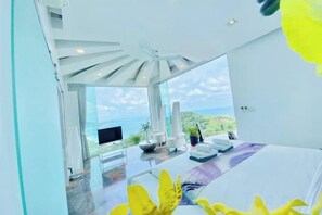 A modern hotel room with a large window, a flat-screen TV, and a seating area with a view of the landscape. - Best World Vision (Koh Samui)