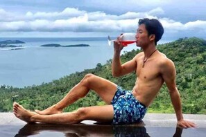 A person sitting by a reflective surface with a scenic view of a body of water and greenery. - Best World Vision (Koh Samui)