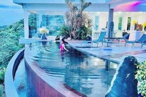 A pool with a waterfall feature, surrounded by lounge chairs and a glass-enclosed area with plants. - Best World Vision (Koh Samui)