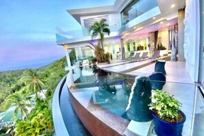 Una moderna casa con piscina a sfioro in vetro, area salotto esterna e vista sul paesaggio.