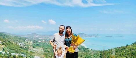 A family on a balcony with a scenic view of a coastal landscape.