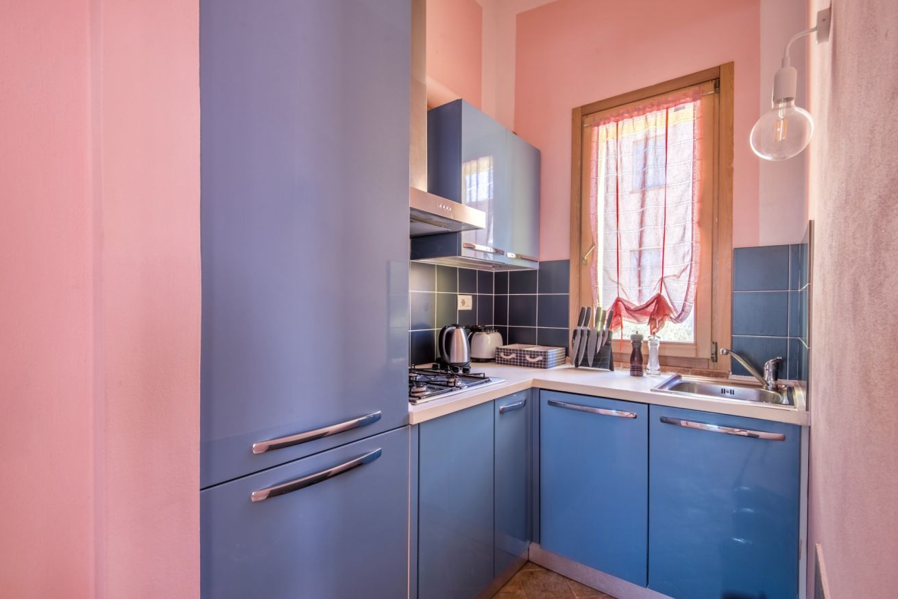 Una cucina compatta con mobili blu, un fornello a gas, un bollitore e una finestra con tende.