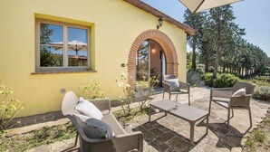 Un edificio amarillo con un arco de ladrillo y una ventana. Hay mobiliario exterior, incluyendo una mesa y sillas.