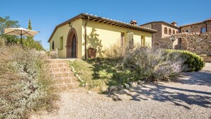 Un edificio de estilo mediterráneo con una escalera de piedra que lleva a una puerta, rodeado de vegetación seca y un cielo despejado.
