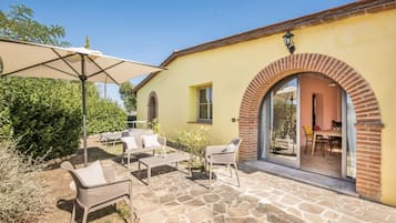 An outdoor patio with stone flooring, wicker furniture, and a large umbrella.