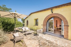 Eine Terrasse im Freien mit Steinboden, Korbmöbeln und einem großen Sonnenschirm.