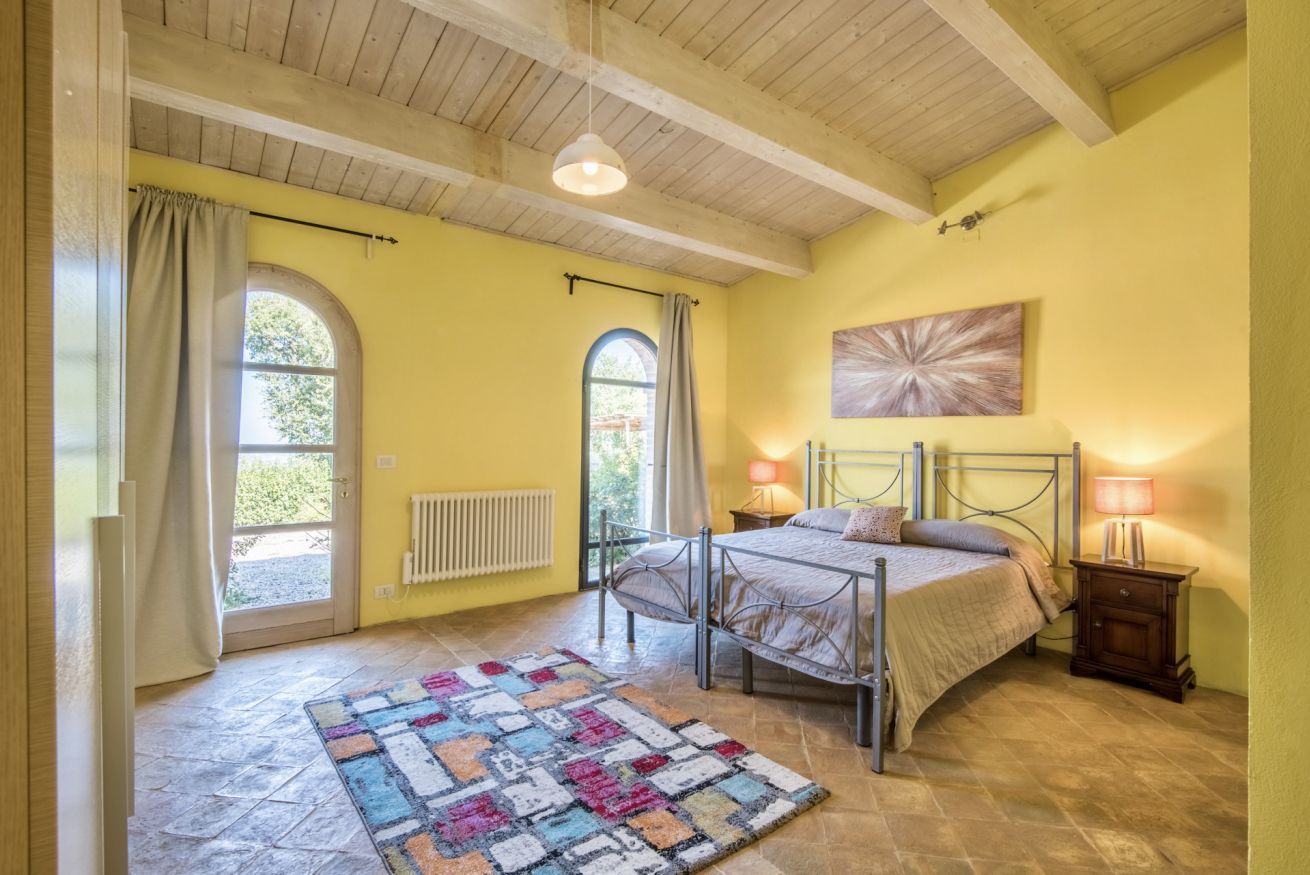 Una camera da letto con un letto, due comodini, un termosifone, una finestra con tende e una ventola a soffitto, oltre a un'opera d'arte appesa al muro.