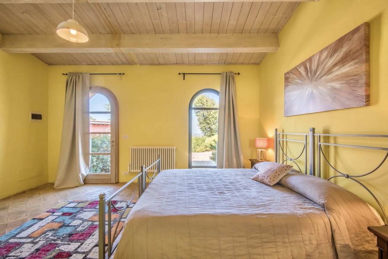 Una camera da letto con un letto, due finestre con tende, un termosifone e un quadro appeso al muro.