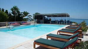 A pool area with lounge chairs and a bar area with umbrellas. - La Perla (Sarandë)