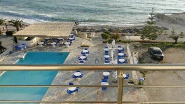 A pool area with blue chairs and umbrellas, a covered seating area, and a view of the ocean. - La Perla (Sarandë)
